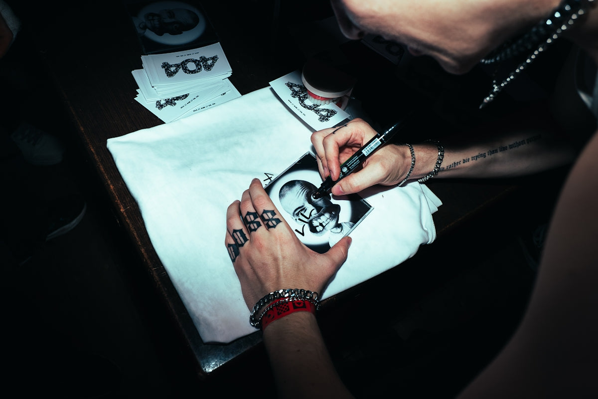 Hands with 'boss' tattoo signing a small photograph.